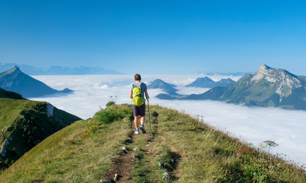 Hiker on a ridge of Mont Trélod on a blue-sky day. He is above the clouds and surrounded by mountain peaks in the French Alps.