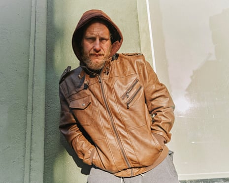 A man in a hooded leather jacket stands for a portrait