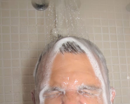 A man's head in the shower with shampoo in his hair
