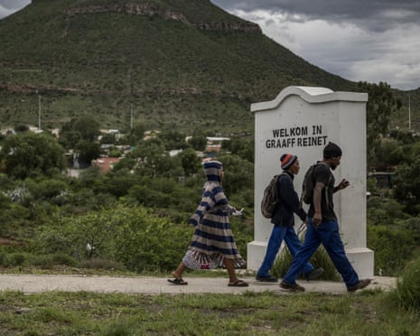 Three people walk past large white stone sign that says Welkom in Graaff Reinet