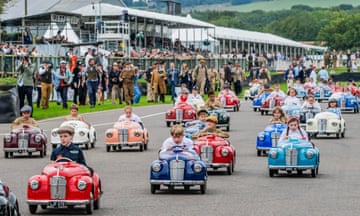 Young drivers on a track in pedal cars with a crowd of supporters behind