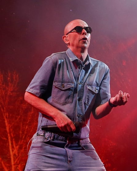 Solari performing in 2017: he is bald and wears black sunglasses, a short-sleeved denim shirt and jeans, and holds a microphone.