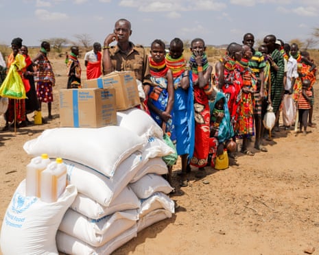 People queue behind large bags and boxes piled up outdoors