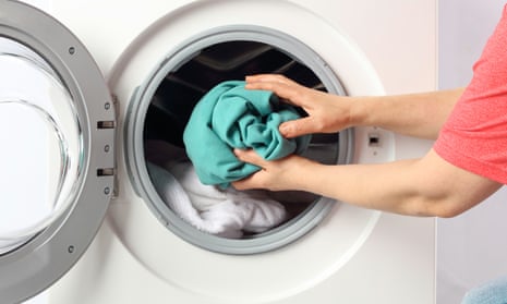 Hands putting a green garment into a washing machine