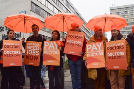 Doctors with orange signs and orange umbrellas protest outside a hospital