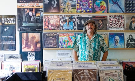 A shop owner stands behind a display of vinyl for sale
