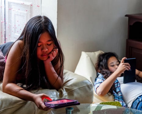 two tween girls sitting in living room on cellphones