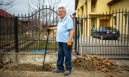 An older man takes a break from raking leaves outside the gates of his home