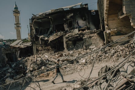 A man walks along a road between piled-up rubble and destroyed buildings