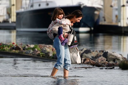 woman walks through floodwater with young girl on her back