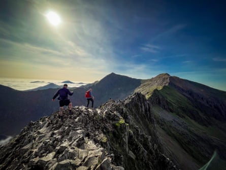 Two men walk on a craggy ridge in strong sunlight
