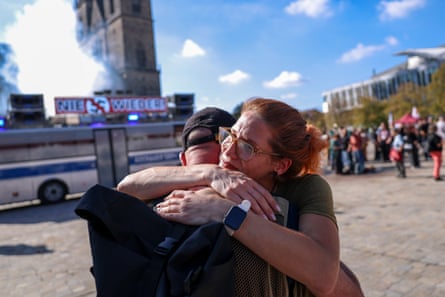 Protesters console each other in front of a bus carrying an anti-Nazi slogan
