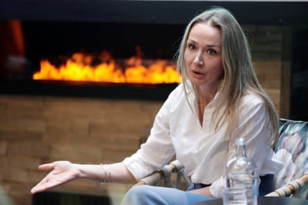 A woman wearing a white shirt gestures as she talks, siting in front of a fire.