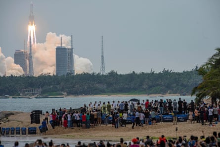 A crowd of people watch as a rocket takes off in the background