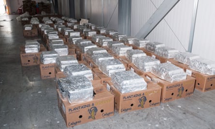Dozens of banana boxes lined up on the floor of a warehouse with silver packages sat on top of them