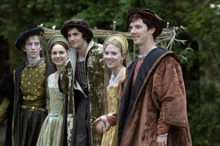 Three men and two women in elaborate Tudor dress stand smiling in a line.