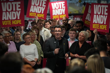 Andy Burnham delivers a speech surrounded by supporters and placards.