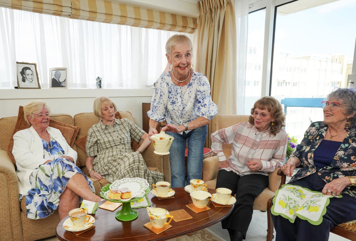 Five women sitting in a living room having tea and cake
