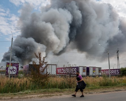 A Wildberries employee walks past a plume of smoke rising from a fire
