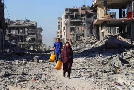 A man and a woman carrying orange bags walk past destroyed buildings in Gaza City