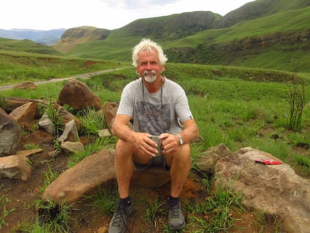 Art Borkent sits on a rock in a hilly green landscape.