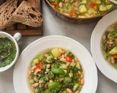 Rachel Roddy’s summer minestrone with pesto – A white bowl of bean and vegetable minestrone topped with pesto and a basil leaf