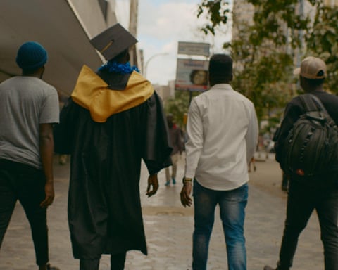 Four men, one in a graduation cap and gown, walk along a street
