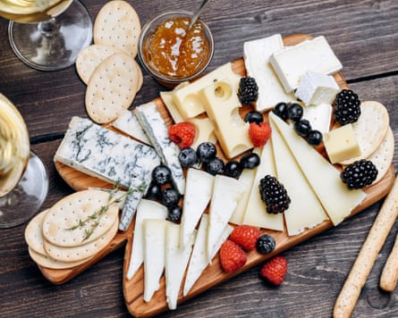 Gorgonzola, parmesan, brie, camembert and maasdam cheeses served with berries and crackers on a wooden board.