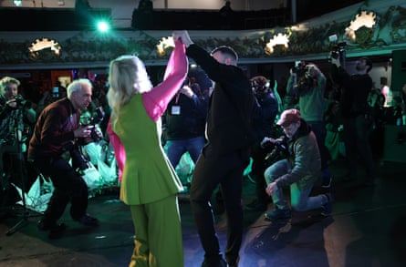 Hannah Spencer and Zack Polanski raise their hands together in front of supporters as photographers gather around