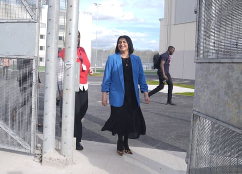 Shabana Mahmood wearing a blue blazer over a long black dress, walks through an open prison gate. dqxikeidqkikdinv