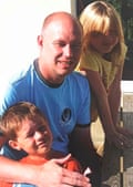 Michael Mullins smiles while posing with a young boy and girl outdoors in sunlight
