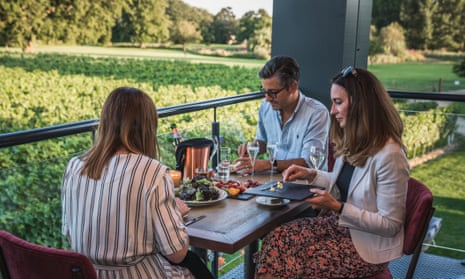 Visitors to the Ashling Park Estate vineyard in Sussex, UK, sit around a table on a veranda drinking wine and eating.