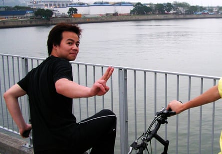 A man on a bike on a bridge turns and makes a V-sign