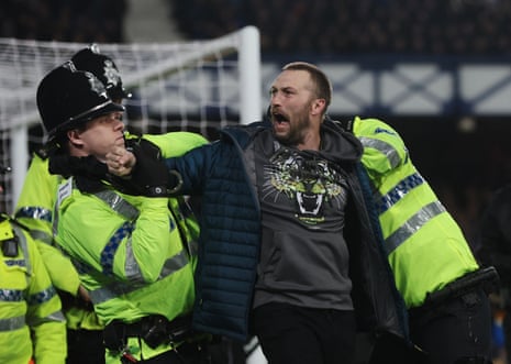 Police officers remove a pitch invader who was protesting against a protester who tied himself to the goal.
