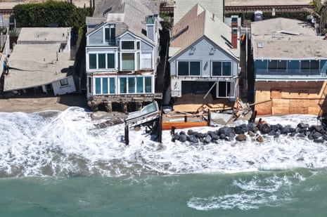 Aerial view of waves crashing against damaged Dana Point beachfront homes with exposed foundations