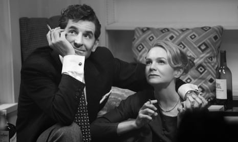 A monochrome image of Bradley Cooper as Leonard Bernstein and Carey Mulligan as Felicia Montealegre sitting together in a domestic setting.