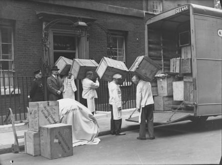 Black and white photo of a team of men in a line carrying out wooden packing crates to a van outside No 10