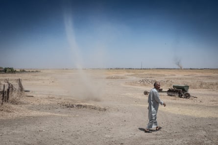A man walks past a dust devil, a rotating column of hot air, in a dry landscape. Another can be seen on the horizon