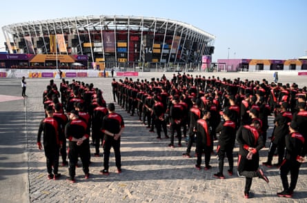 Rows of men dressed in black and red uniforms line up in front of a stadium