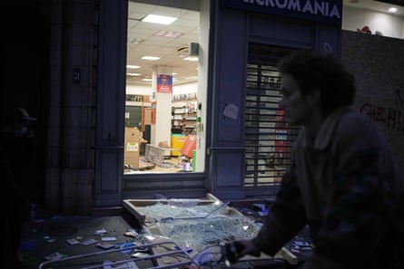 A man rides past a looted shop in Lyon, with a smashed door and debris on the pavement