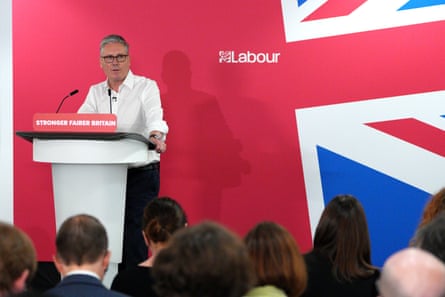 Keir Starmer speaks to an audience from a podium in front of a giant union jack flag with a section of red and the Labour logo behind him.
