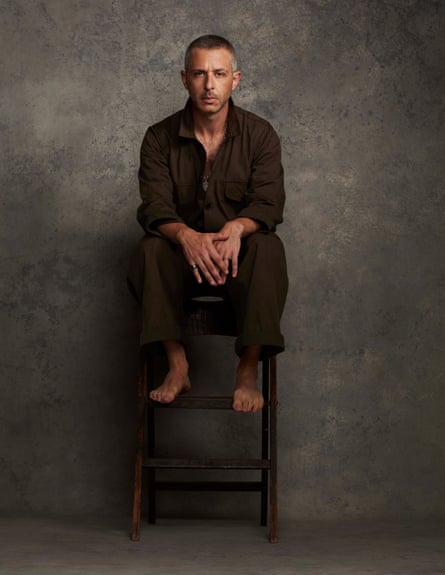 Jeremy Strong sitting on a high stool wearing an olive green jumpsuit