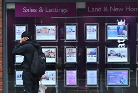 Someone looks at houses for sale in the window of an estate agents