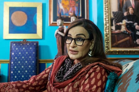 A woman in traditional shalwar kameez and scarf sits in a room full of pictures