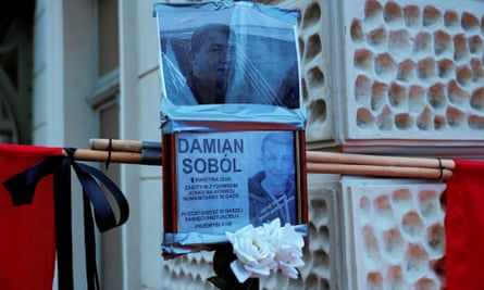 Posters of Damian Sobol are tied to a pole with white flowers and flags