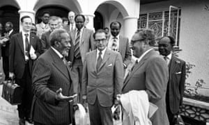 Kissinger talking with an older African man while other black and white officials stand in the background