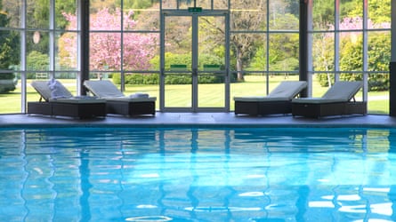 Indoor hotel swimming pool backed by large windows looking out to a spring garden