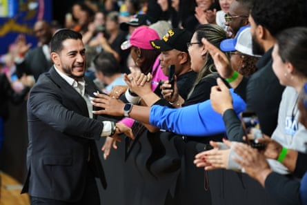 Man in suit smiles and shakes hands as people reach out toward him.