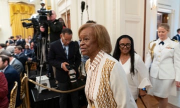 Black woman in white and brown shirt surrounded by press at the White House