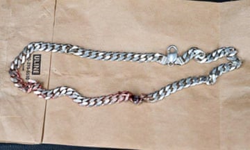 A thick silver chain necklace with blood stains on top of a brown paper bag